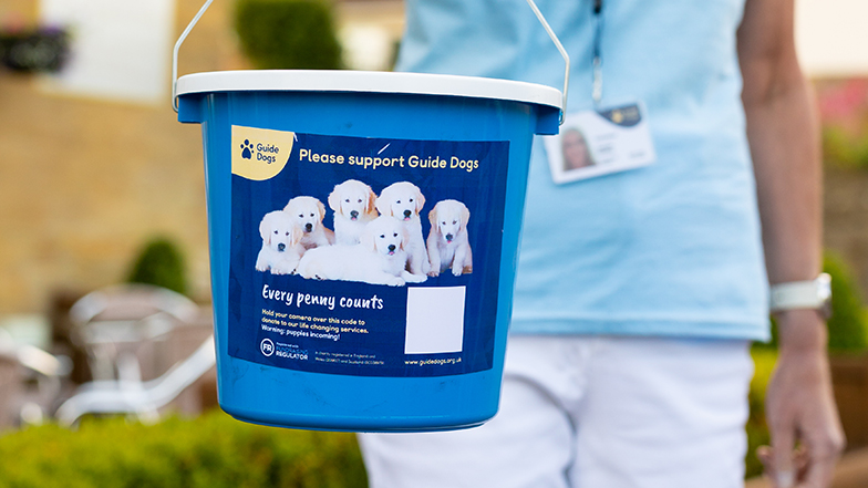 Collection box coordinator showing Guide Dogs donation bucket