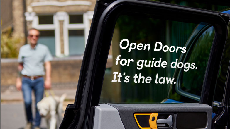 A taxi with the door open with 'Open Doors for guide dogs - It's the law' printed on the window