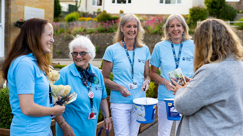 A fundraising group in Guide Dog's t-shirts smile as they collect funds