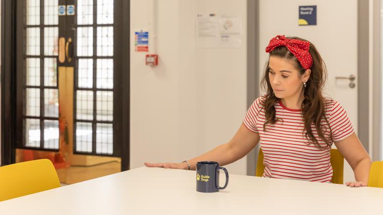 A woman sits at a table and uses both hands to trace the edges nearest to her.