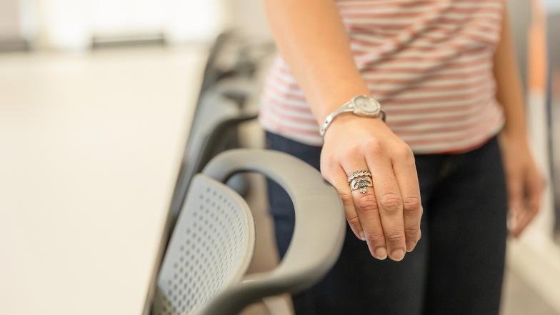 A close up shows someone touching the top of a chair with the side of their hand.